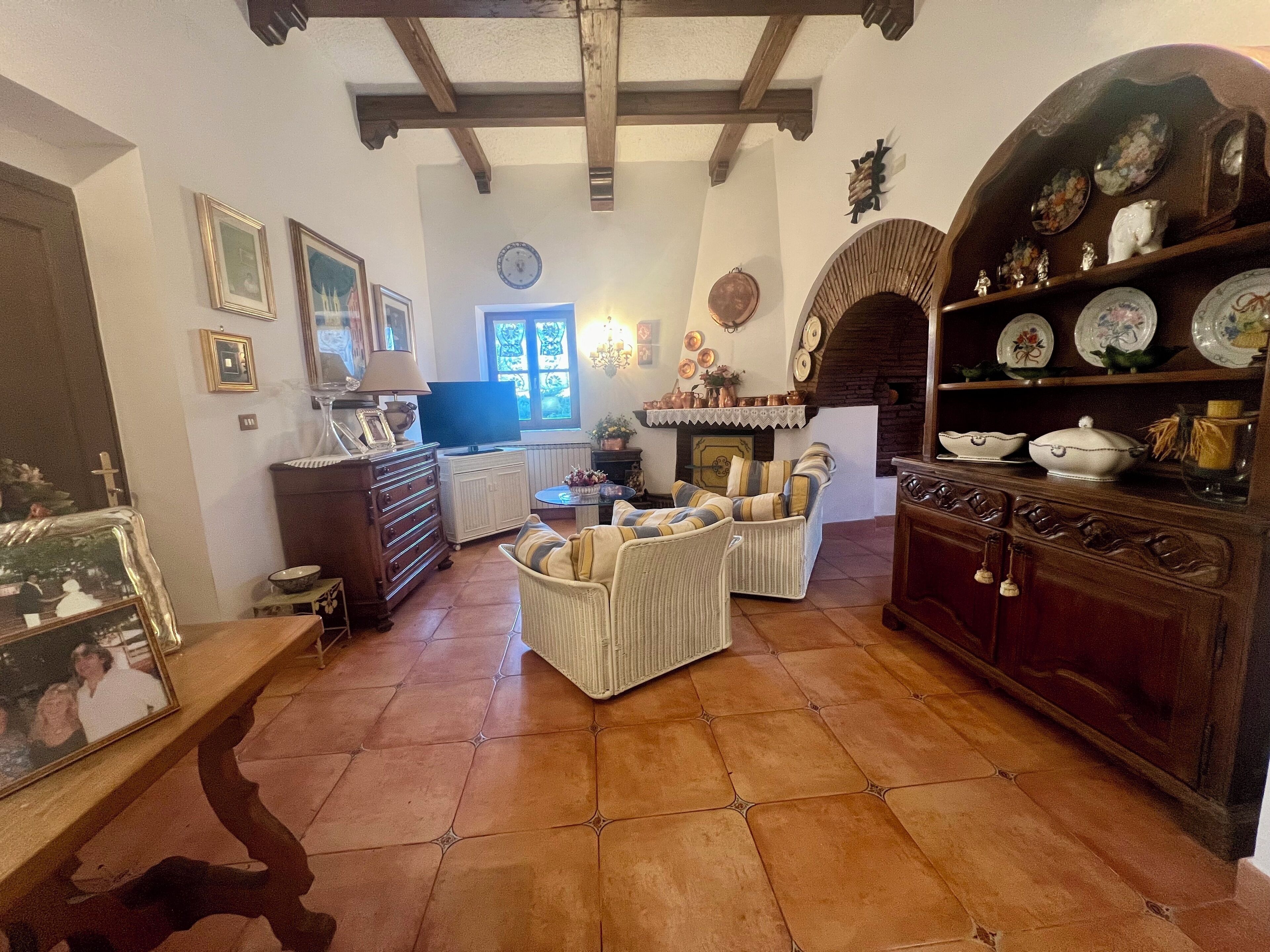 A cozy living room with a fireplace, wicker furniture, and a wooden cabinet with decorative plates.