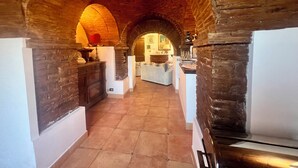 A narrow hallway with arched brick ceilings and a tiled floor, leading to a kitchen area with a counter and seating.