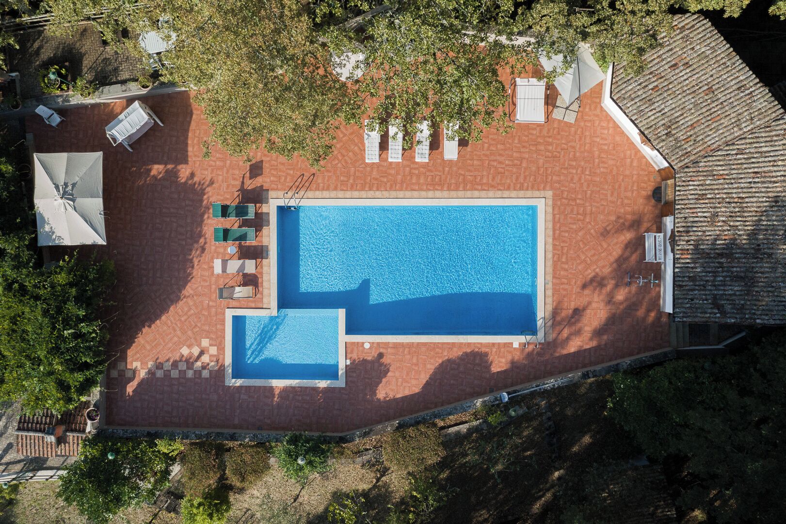 Vista aérea de un área de piscina con una piscina rectangular, una piscina más pequeña contigua y varias sillas de descanso.