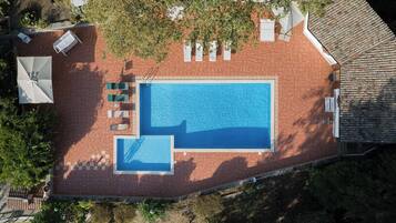 Vista aérea de un área de piscina con una piscina rectangular, una piscina más pequeña contigua y varias sillas de descanso.