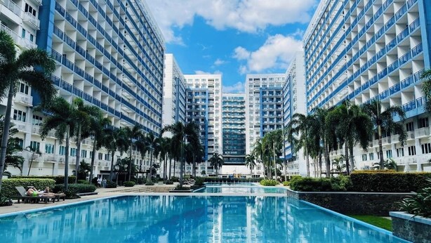 Un hotel con piscina central, rodeado de palmeras y edificios modernos.