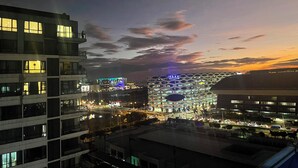 Un paisaje urbano moderno al atardecer, con edificios iluminados y una estructura circular destacada.