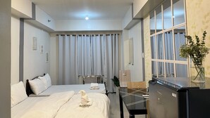 Una habitación de hotel con cama, escritorio, refrigerador y ventana con cortinas.