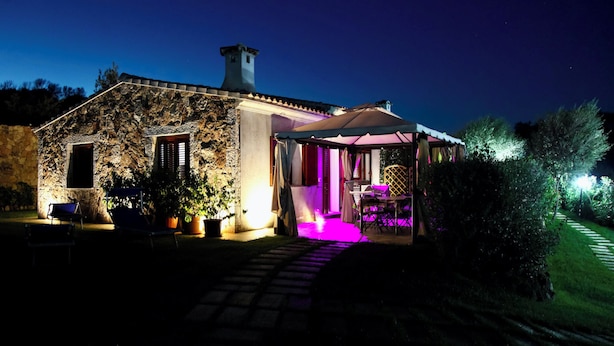 A stone building with a covered patio area, a stone pathway leading to the entrance, and potted plants around the seating area. - Stazzu Fioritu trilocali vista mare (San Teodoro)