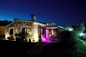 A stone building with a covered patio area, a stone pathway leading to the entrance, and potted plants around the seating area. - Stazzu Fioritu trilocali vista mare (San Teodoro)