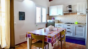 A kitchen with white cabinets, a tiled backsplash, and a table with a colorful tablecloth. - Stazzu Fioritu trilocali vista mare (San Teodoro)