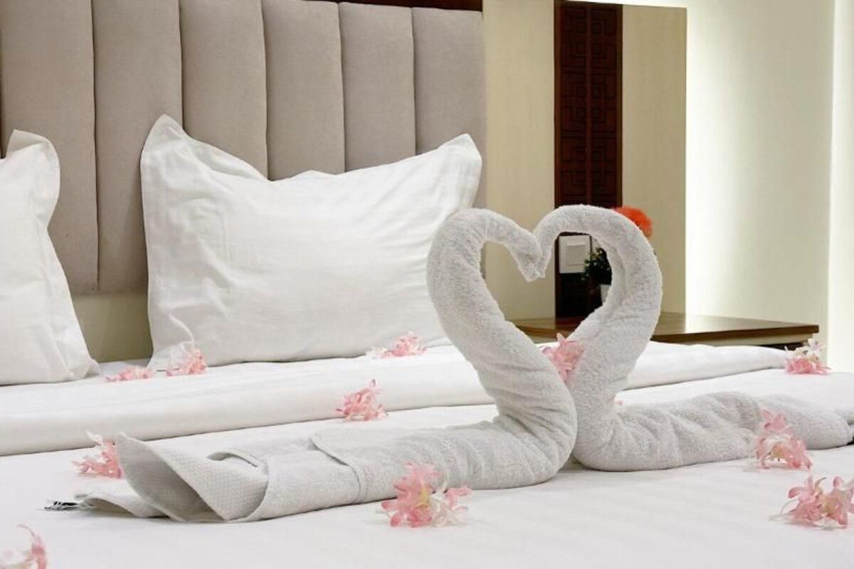 A neatly made bed with white linens and a heart-shaped towel arrangement.