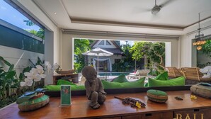 Zona de recepción con mostrador de madera, una estatua y vistas a una piscina y área de estar al aire libre.