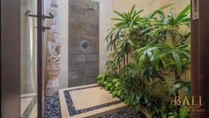 Una zona de ducha con una escultura de piedra, un muro con azulejos y una planta en maceta.