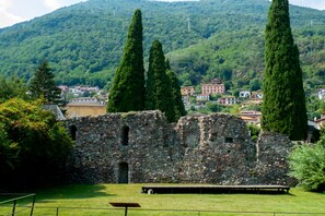 Un bâtiment historique en pierre, avec une pelouse en premier plan et une chaîne de montagnes en arrière-plan.