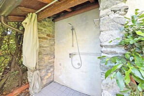 Zona de ducha con paredes de piedra, un cabezal de ducha metálico y una toalla colgada de un gancho.