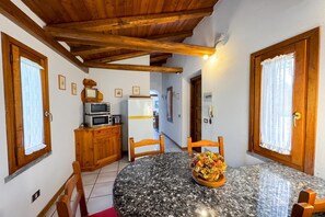 Un pequeño comedor con una mesa redonda, sillas, microondas, refrigerador y armarios de madera.