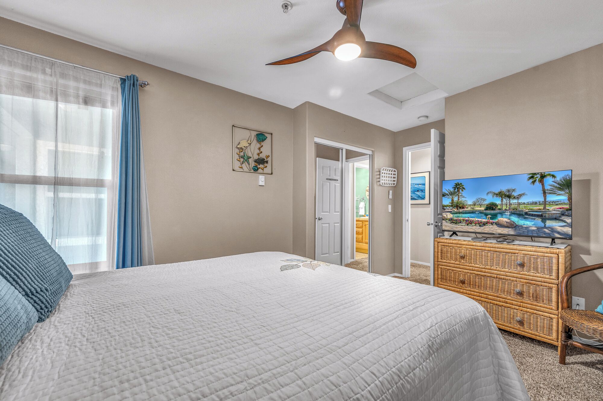 A bedroom with a large bed, a ceiling fan, a television, and a door leading to another room.