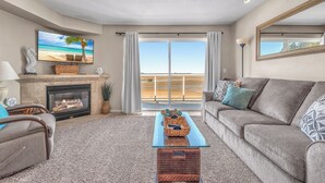 A living room with a fireplace, a sofa, a coffee table, and a large window with a view of a beach. - Top Floor, Ocean View Condo in The Heart of The Taft District in Lincoln City (Lincoln City)