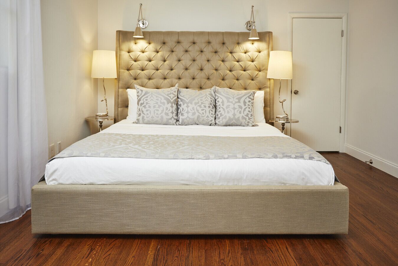 A large bed with a tufted headboard, two bedside lamps, and a neutral color scheme.