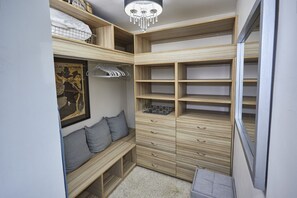 A walk-in closet with wooden shelving, drawers, and a bench with pillows.