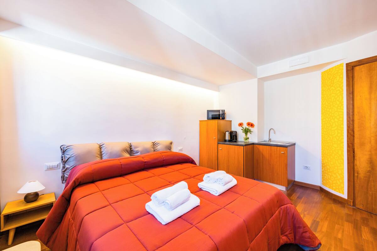 A hotel room with a bed, a nightstand, a desk with a sink, and a wardrobe.