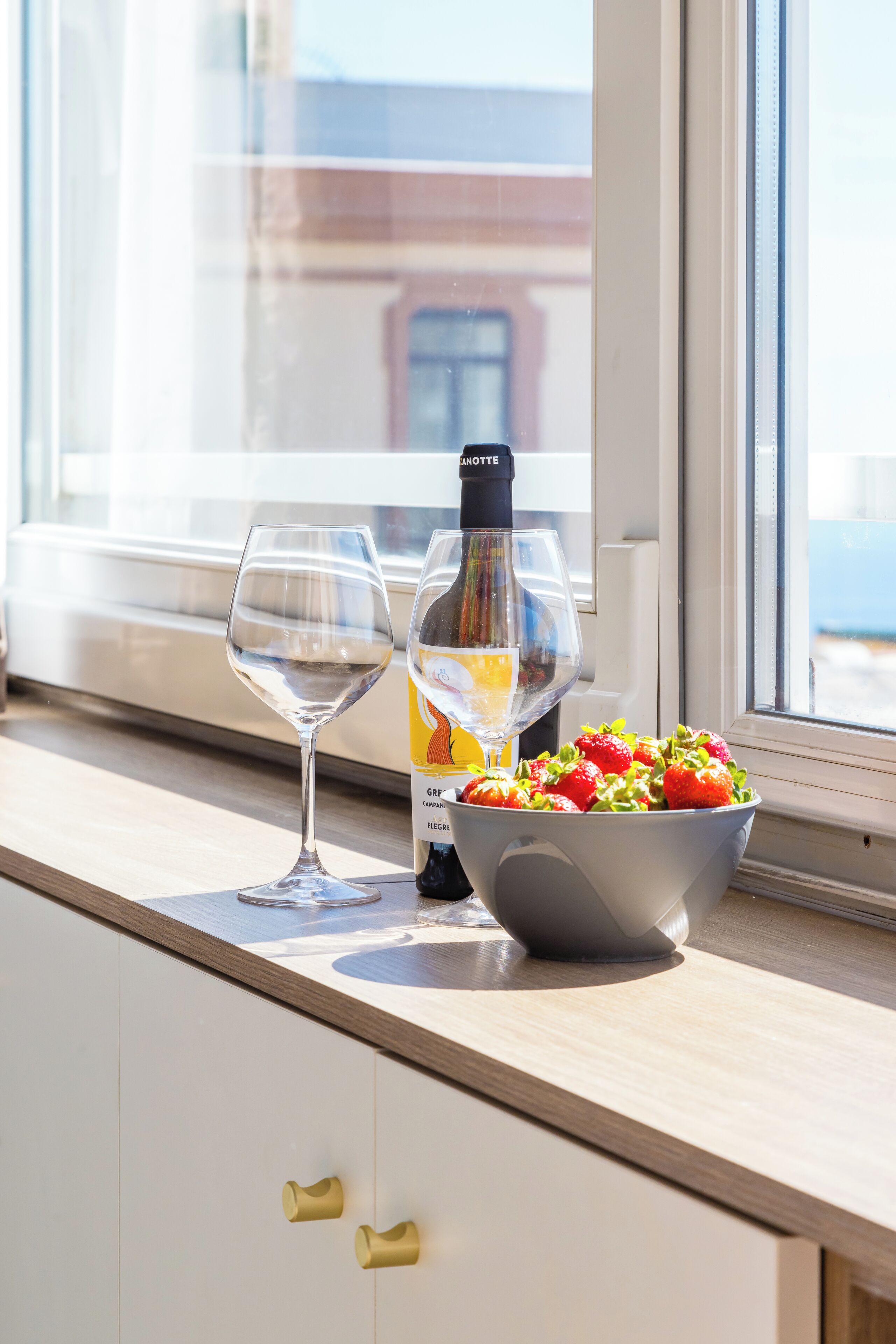 A kitchen counter with a bowl of strawberries, a bottle of wine, and a wine glass.