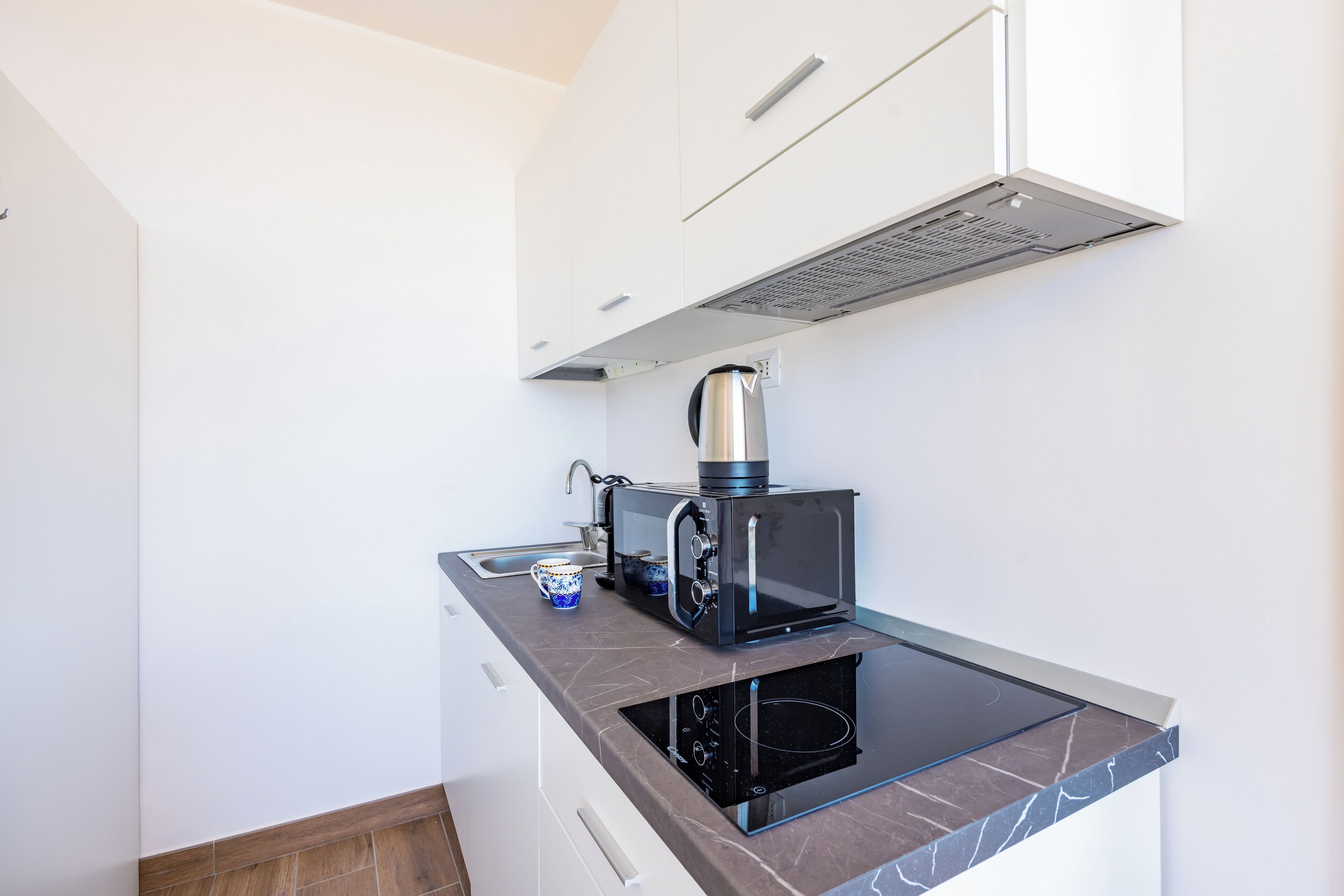 A compact kitchen with a built-in microwave, a kettle, and a small sink.