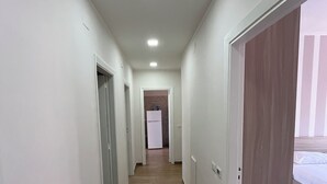 Un couloir d’hôtel avec un plancher en bois, des murs blancs et une porte donnant sur une chambre à coucher où se trouve un lit.