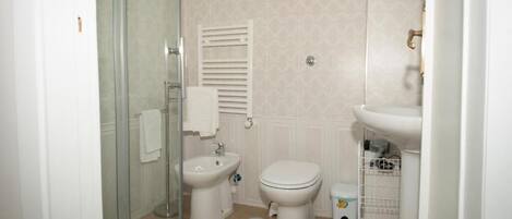 Un baño pequeño y funcional con cabina de ducha de vidrio, inodoro, bidé y lavamanos.