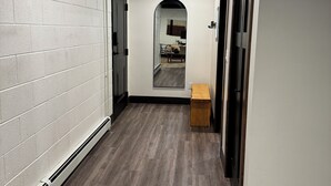 Un couloir aux murs en briques blanches, avec un banc en bois et une arche ornée de miroirs qui mène à une pièce.