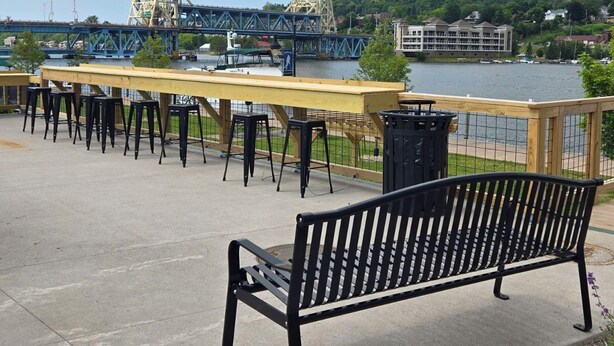 Une terrasse au bord de l’eau, avec un banc, des tables et des chaises.