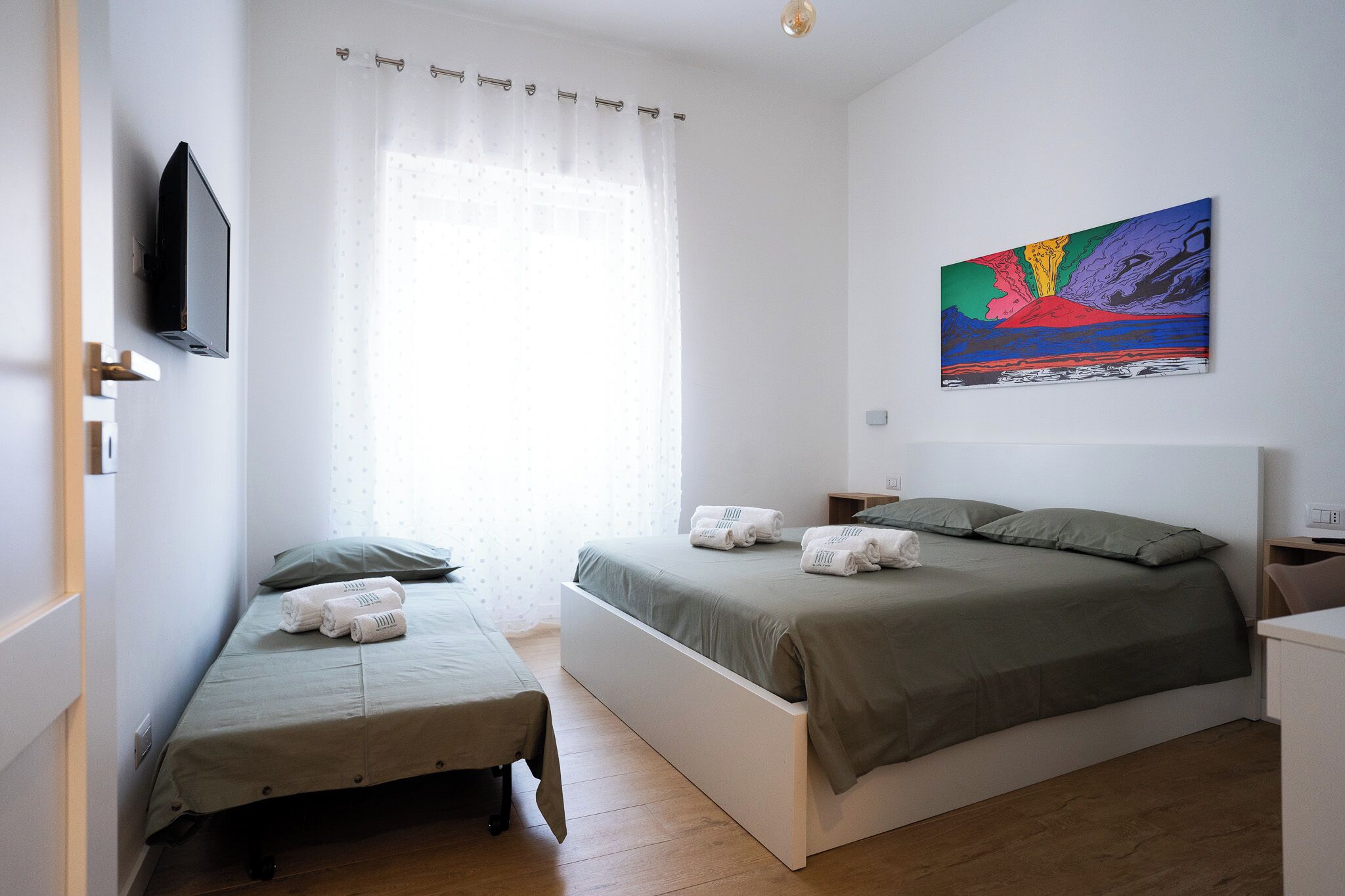 Une chambre à coucher avec un lit, un petit lit, une télévision et un tableau accroché au mur.