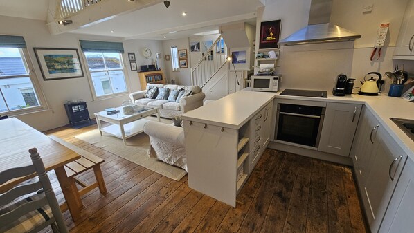 A modern kitchen with a built-in oven and microwave, a dining area with a wooden table and chairs, and a living room with a sofa and a coffee table.