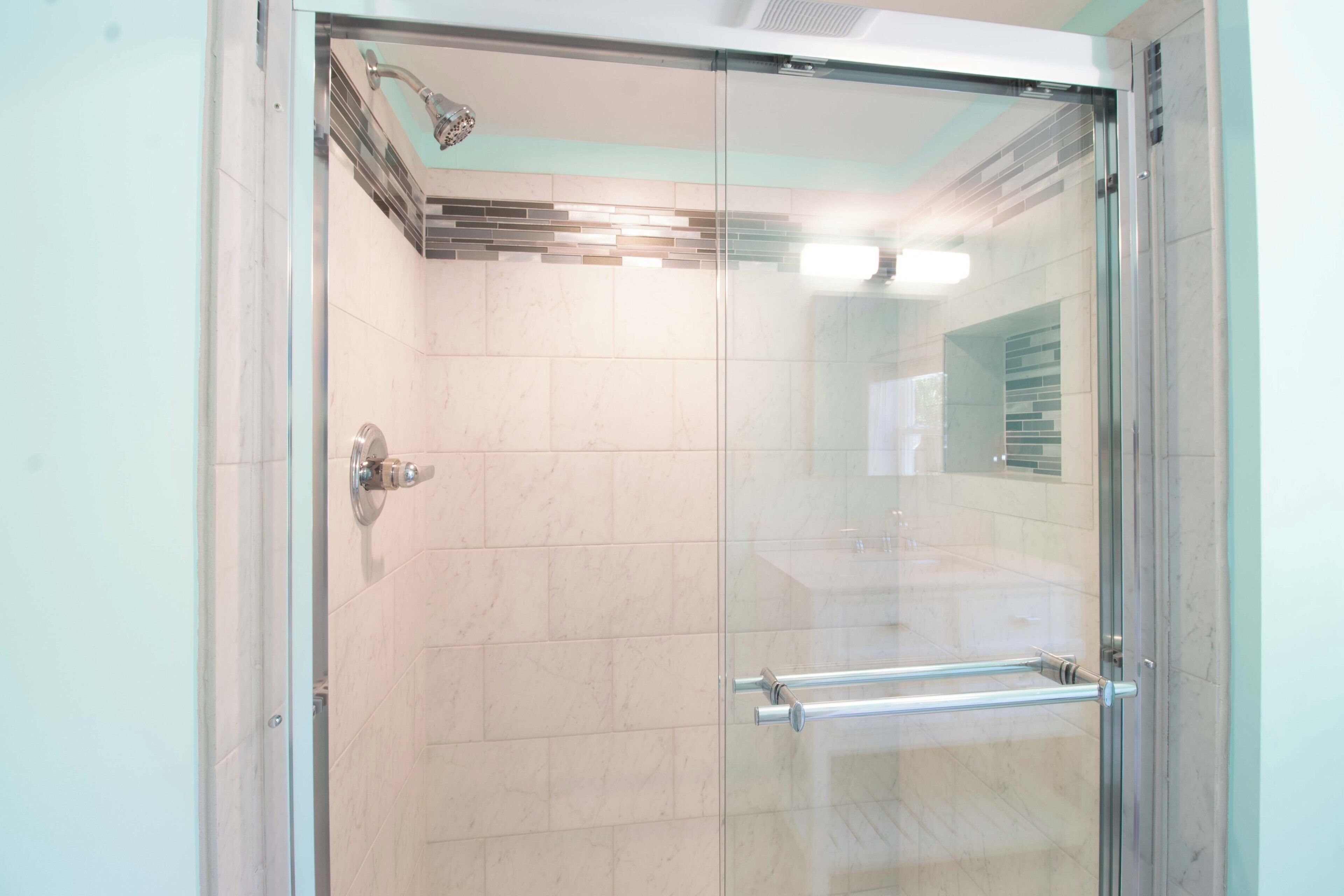 A glass-enclosed shower with a tiled wall, a visible showerhead, and a handrail.