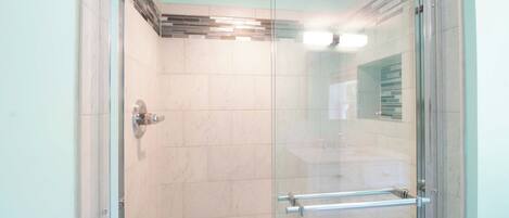 A glass-enclosed shower with a tiled wall, a visible showerhead, and a handrail.