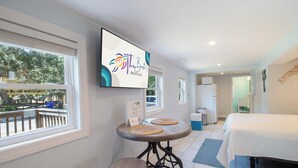 Une chambre d’hôtel avec un lit, une table avec deux sets de table, un téléviseur fixé au mur et une fenêtre donnant sur l’extérieur.