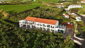 Um edifício branco com telhado vermelho, cercado por vegetação exuberante e campos.