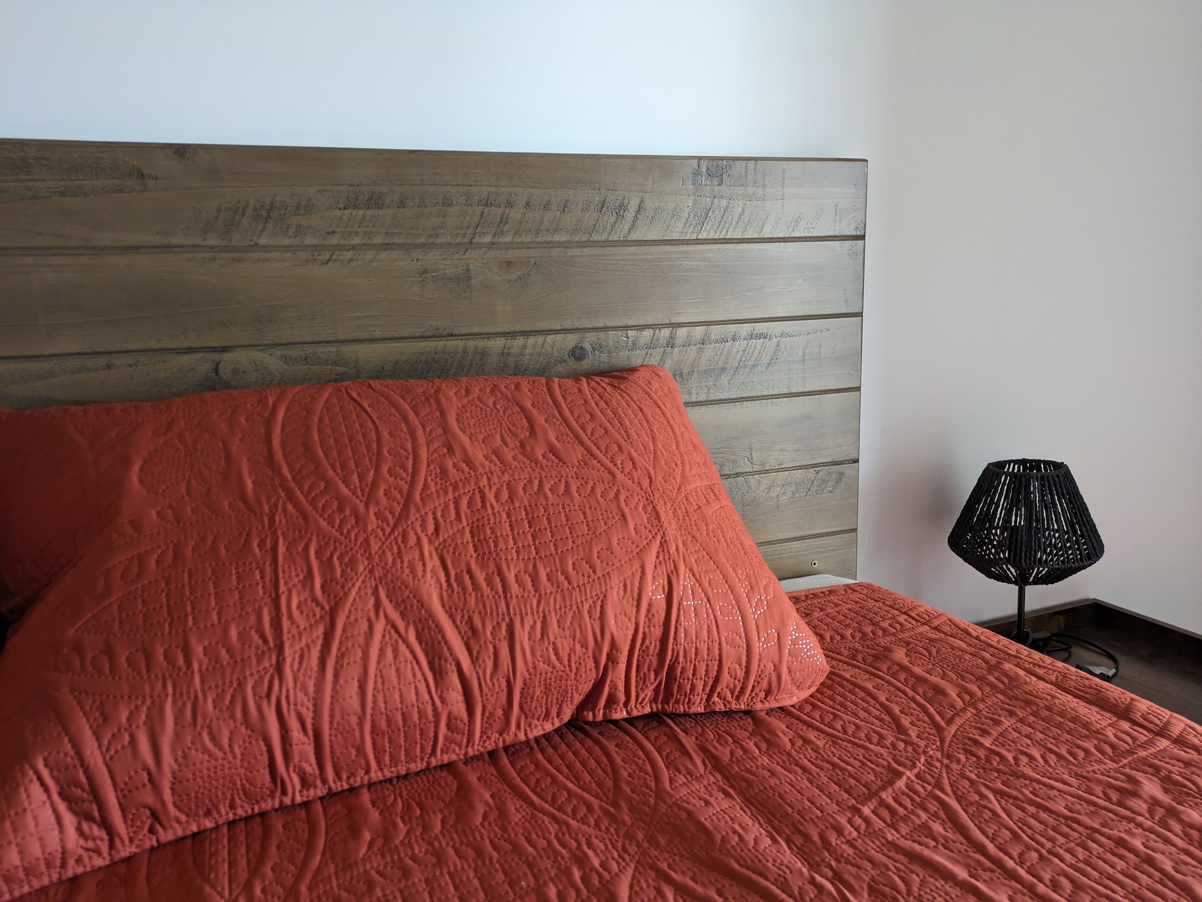 A bed with a wooden headboard and a red quilted bedspread.