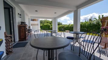 An outdoor patio area with round tables and chairs, a wooden cabinet, and a view of the garden.