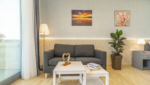 A modern living room with a grey sofa, a white coffee table, a potted plant, and two wall-mounted lamps. - Amour Relax Hotel (Apokoronas)