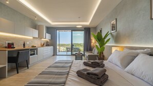 A modern hotel room with a large bed, a desk, and a balcony with a view. - Amour Relax Hotel (Apokoronas)