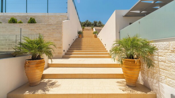 A staircase leading up to a building with a modern design, flanked by large planters with greenery. - Amour Relax Hotel (Apokoronas)