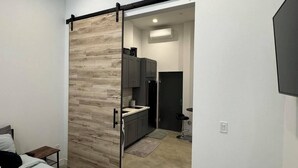 A modern bedroom with a bed, a sliding door leading to a kitchen, and a TV mounted on the wall. - Cozy studio in enchanting Seattle with AC, WiFi (Seattle)