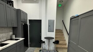 A modern kitchen with grey cabinets, a black refrigerator, and a coffee machine. There are two stools and a small table in the center. - Cozy studio in enchanting Seattle with AC, WiFi (Seattle)