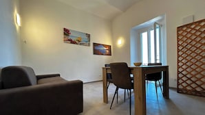 Een woonkamer met een bank, een eettafel met stoelen, en twee schilderijen aan de muur.