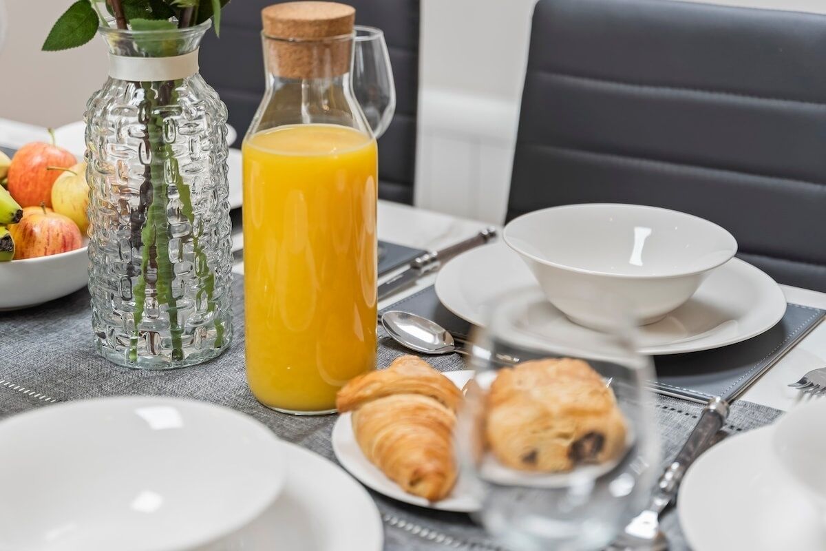 Une table dressée pour le petit-déjeuner avec des croissants, un verre de jus d’orange et un bol de fruits.