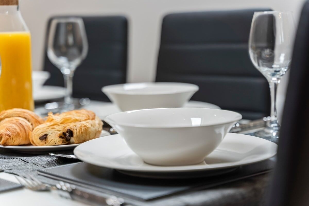 Une table mise pour le petit-déjeuner, avec des croissants et un verre de jus d’orange, ainsi que des bols blancs et des verres à vin.