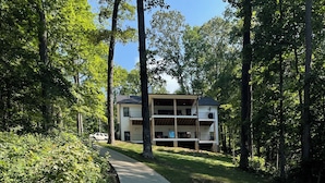 A concrete pathway leading to a multi-story building with balconies, surrounded by trees and greenery.
