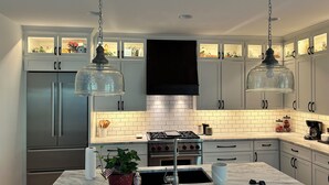 A modern kitchen with grey cabinets, a central island, stainless steel appliances, and pendant lighting.