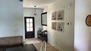 A dining area with a dark wooden table and white chairs, a black door with a window, and a chandelier.