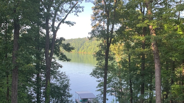 A lakeside view from a deck with a boat dock, surrounded by trees and a grassy area.