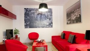 A modern living room with a red sofa, a red chair, a small table, and a TV on a stand.