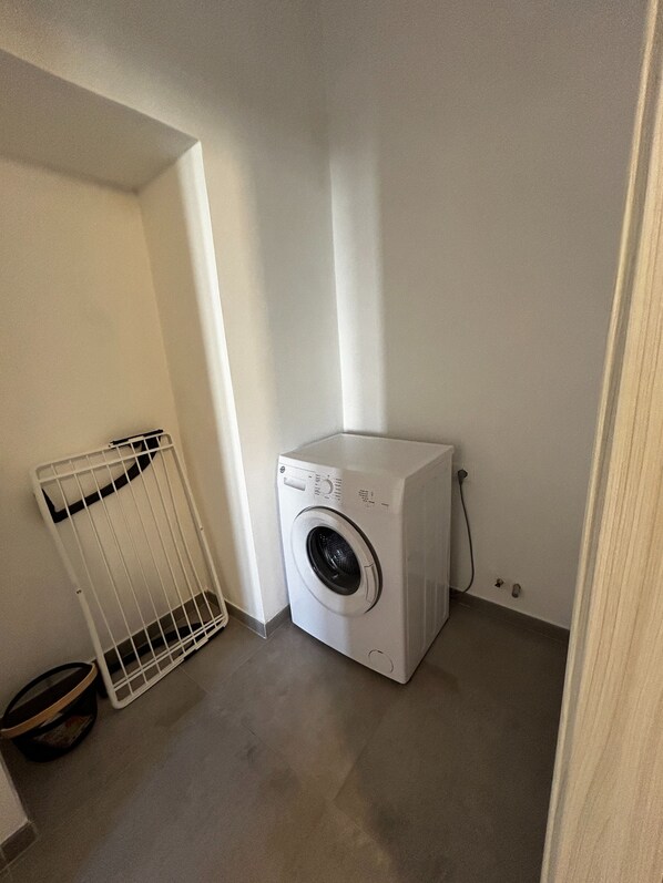 A small laundry room with a washing machine, a drying rack, and a floor drain.