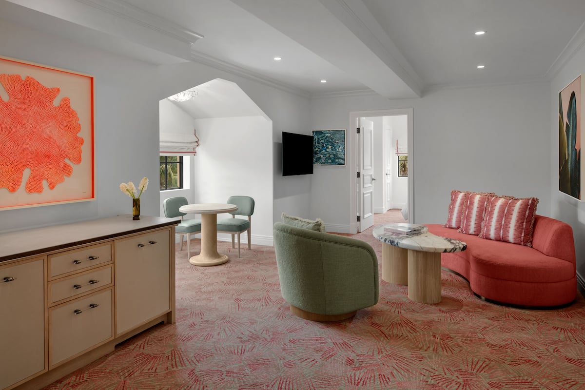 A modern living room with a sofa, armchair, and a coffee table. There is a TV mounted on the wall and a large artwork on the wall.